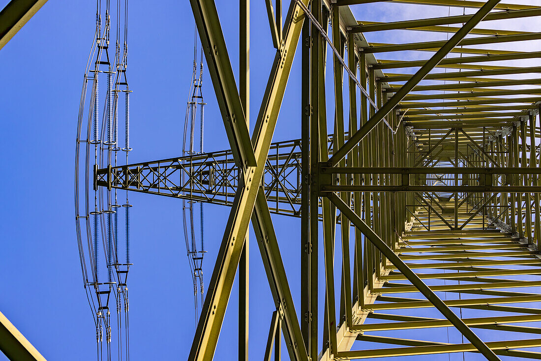  Complex steel structure with trusses and cross braces of a high voltage pylon with suspension for power lines seen from below 