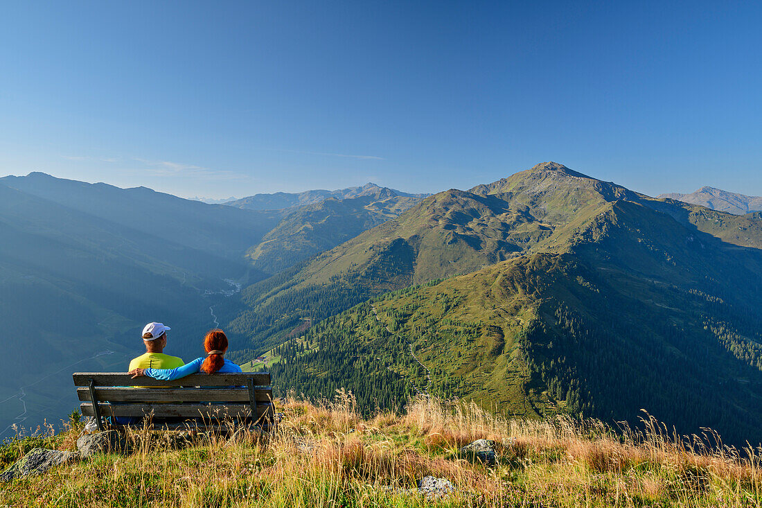  Man and woman hiking sitting on bench and looking at Gilfert, Kuhmesser, Tux Alps, Tyrol, Austria 