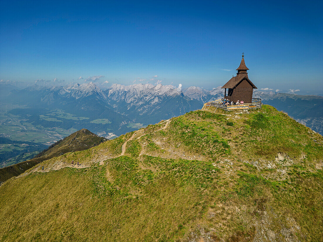 Mehrere Personen sitzen an der Kapelle am Gipfel des Kellerjochs, Inntal und Karwendel im Hintergrund, Kellerjoch, Tuxer Alpen, Tirol, Österreich
