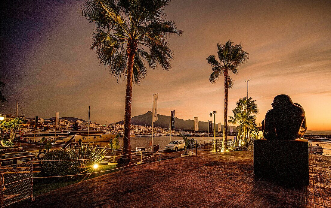  Sculpture by Jiménez Deredia on the seafront of Puerto Banús with a view of the marina at sunrise and dawn, Costa del Sol, Andalusia, Spain 