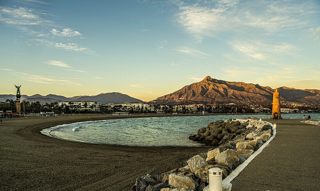  Beach and promenade of Puerto Banús in the evening light, in the background the Sierra Blanca and the Victoria statue, Marbella, Costa del Sol, Spain 
