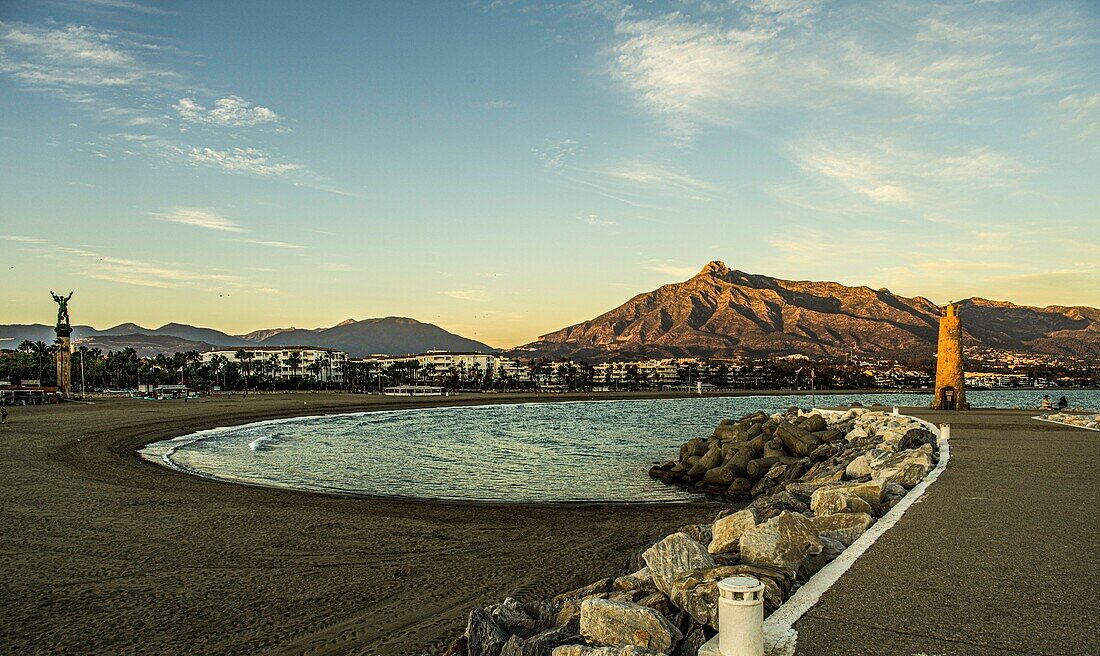 Strand und Strandpromenade von Puerto Banús im Abendlicht, im Hintergrund die Sierra Blanca und die Victoria-Statue, Marbella, Costa del Sol, Spanien