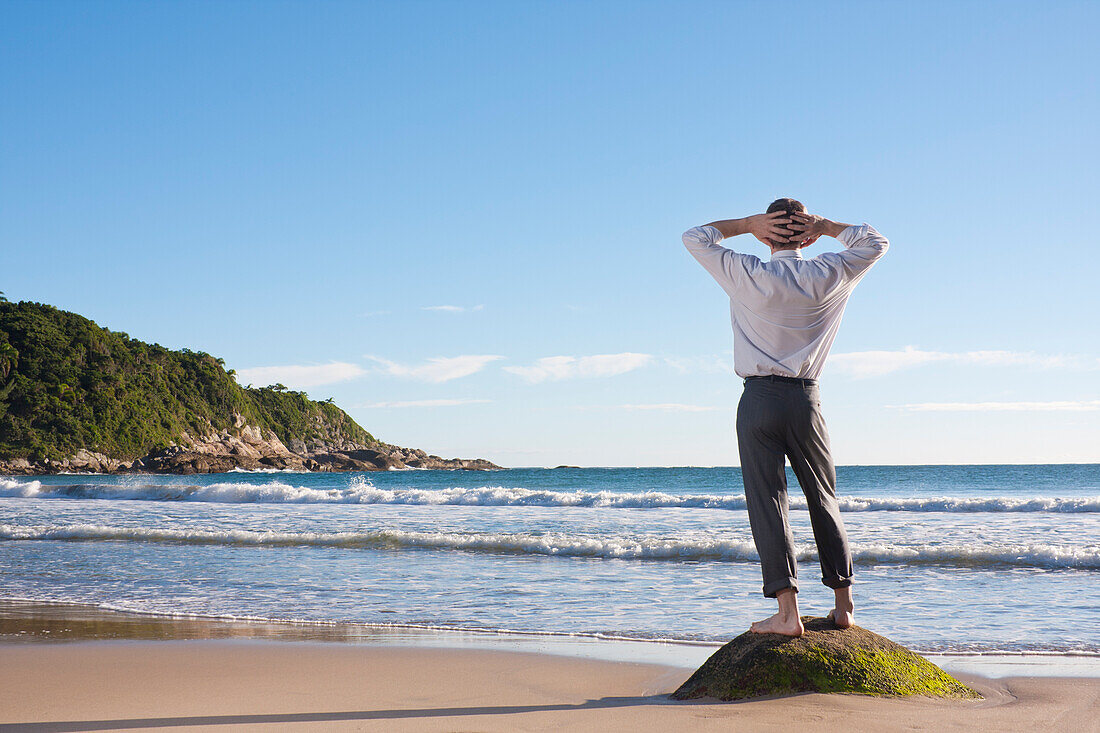 Geschäftsmann steht barfuß auf einem Felsen am Strand und entspannt sich, Bombinhas, Santa Catarina, Brasilien