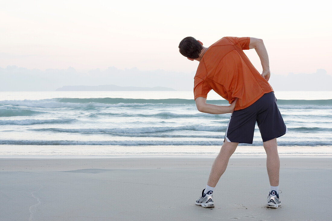  Runner doing stretching exercises on the beach, Bombinhas, Santa Catarina, Brazil 