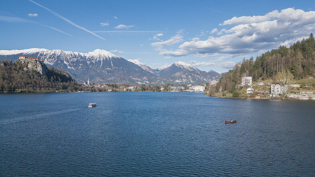 Blick über den Bleder See auf die Burg und die dahinter liegenden verschneiten Berge in Bled, Slowenien, Europa.