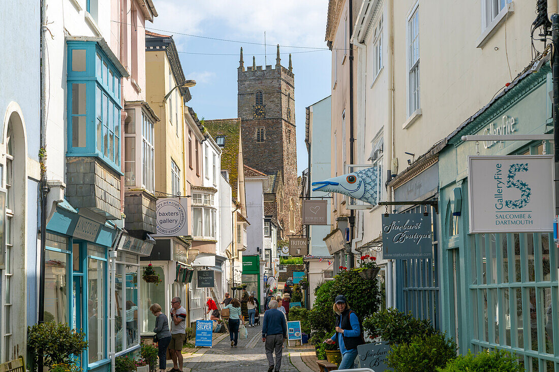 Geschäfte in historischen Gebäuden entlang der Gasse mit Turm der Kirche St. Saviour, Foss Street, Dartmouth, Devon, England, Großbritannien