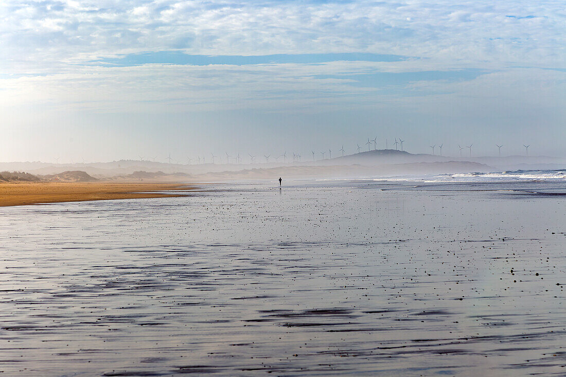 Silhouette figure man running in the distance on wide sandy beach at low tide, Essaouira, Morocco, north Africa