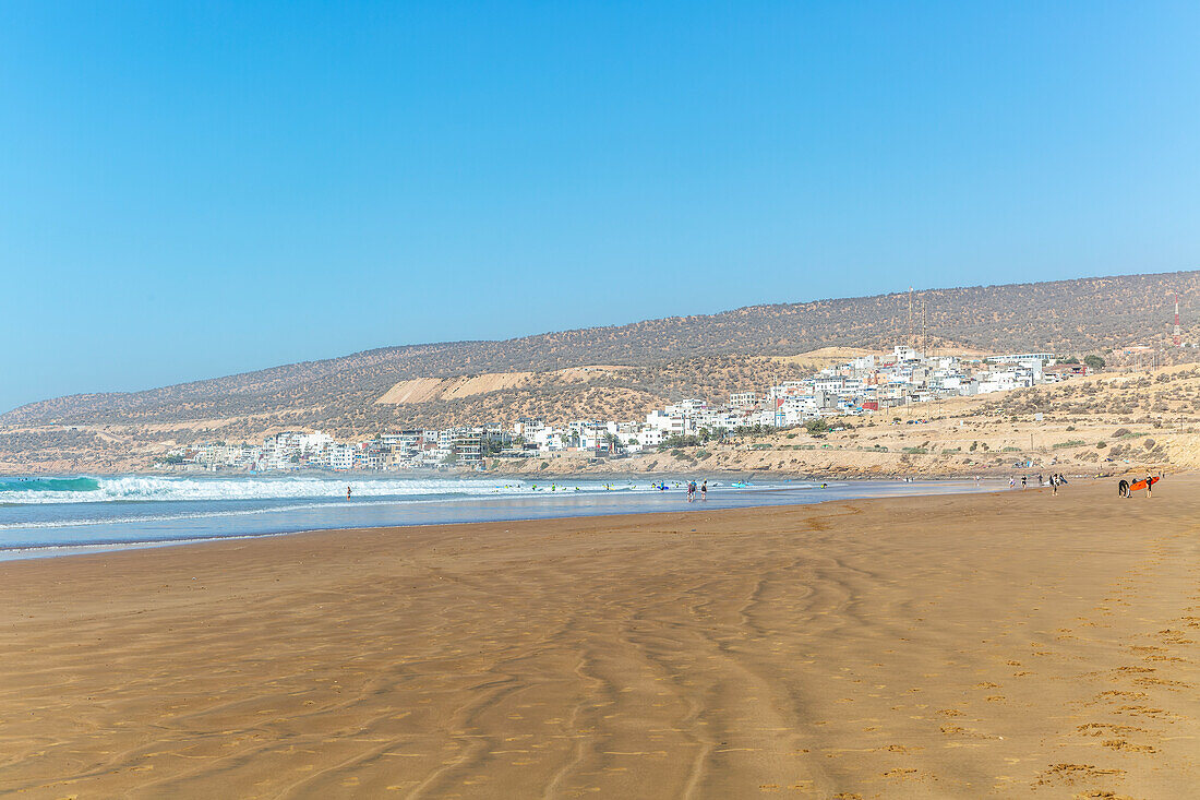 Menschen spazieren bei Ebbe am Sandstrand in der Nähe des Dorfes Taghazout, Marokko, Nordafrika