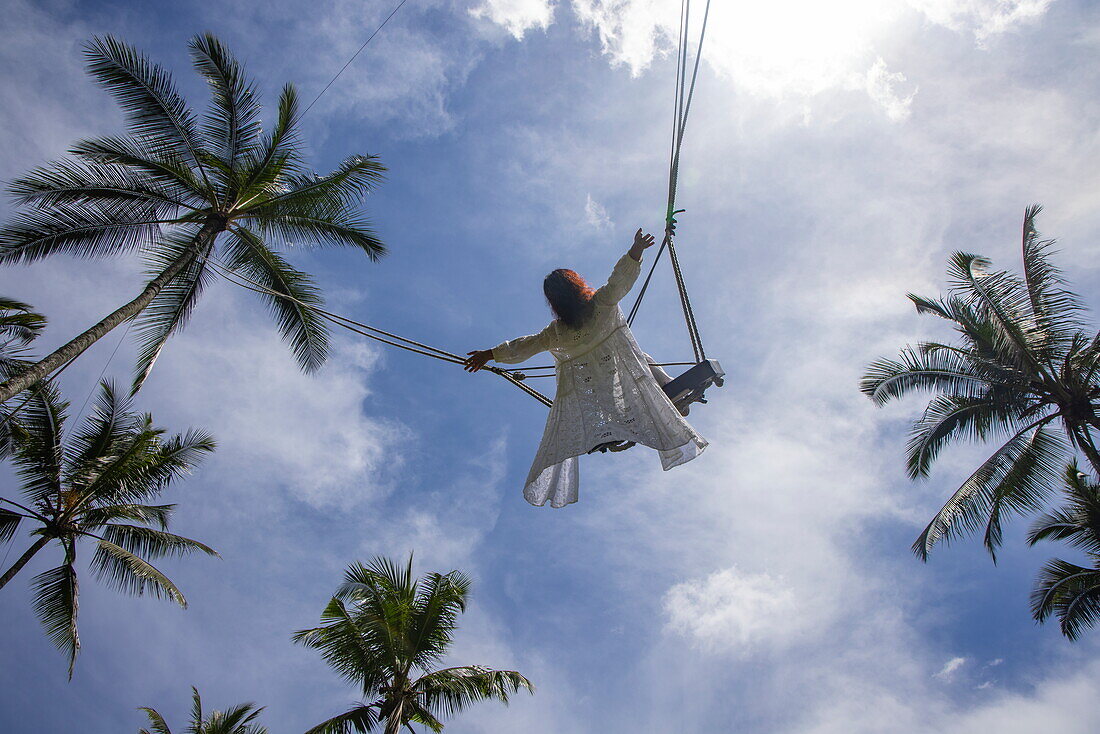 Frau auf Bali-Schaukel zwischen Kokospalmen auf der Tegallalang-Reisterrasse, Tegallalang, Gianyar, Bali, Indonesien, Südostasien