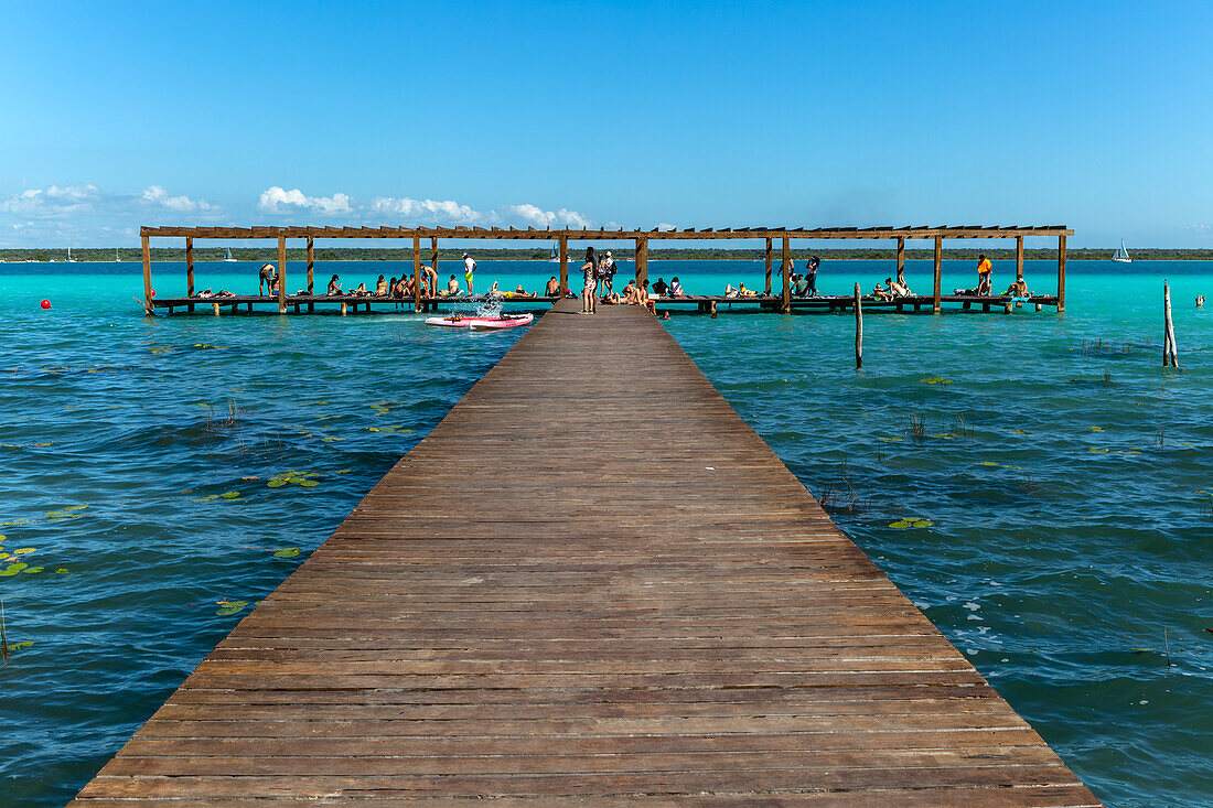 Leute sitzen auf einem hölzernen Anlegesteg am Wasser, See Bacalar, Bacalar, Quintana Roo, Halbinsel Yucatan, Mexiko