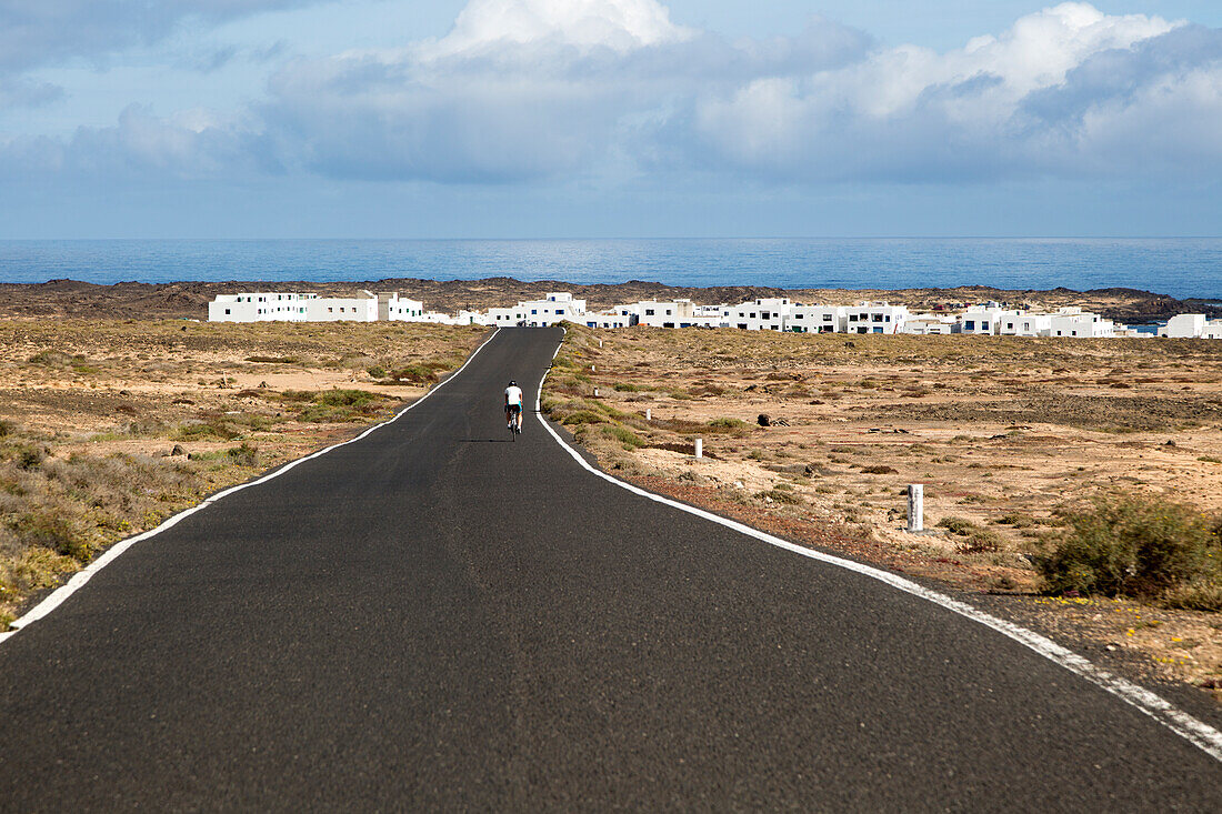 Radfahrer auf der Straße nähert sich dem Dorf Caleta de Caballo, Lanzarote, Kanarische Inseln, Spanien