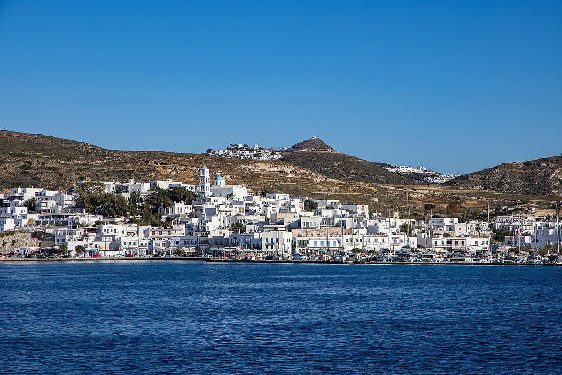 Blick vom Meer auf die Stadt Adamas mit Ort Plaka auf einem Hügel in der Ferne, Adamas, Insel Milos, Kykladen, Südliche Ägäis, Griechenland, Europa