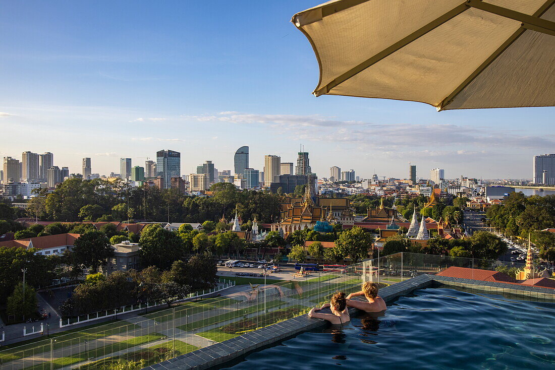 Paar im Infinity-Pool auf dem Dach des Glow Park Hotels mit Blick auf den Königspalast und die Skyline der Stadt, Phnom Penh, Kambodscha, Asien