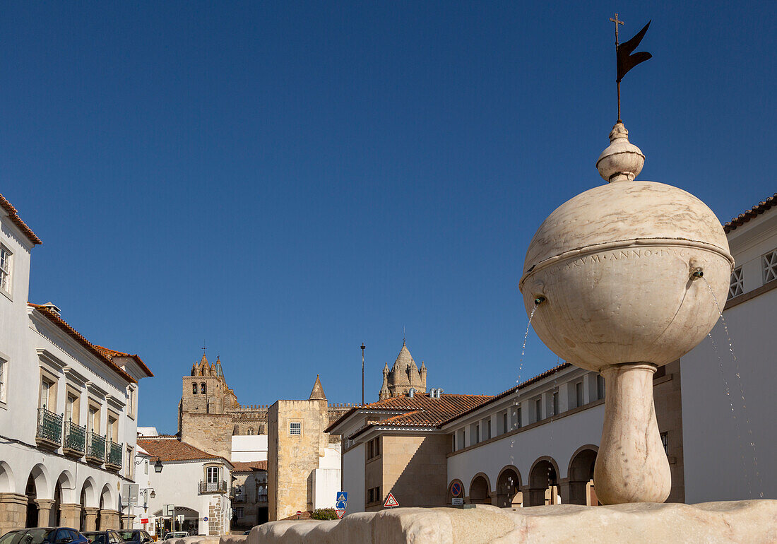 Fountain in the Largo das Portas de Moura with a view to the cathedral and surrounding historic buildings in the city centre of Evora, Alto Alentejo, Portugal, Southern Europe - 23 March 2019