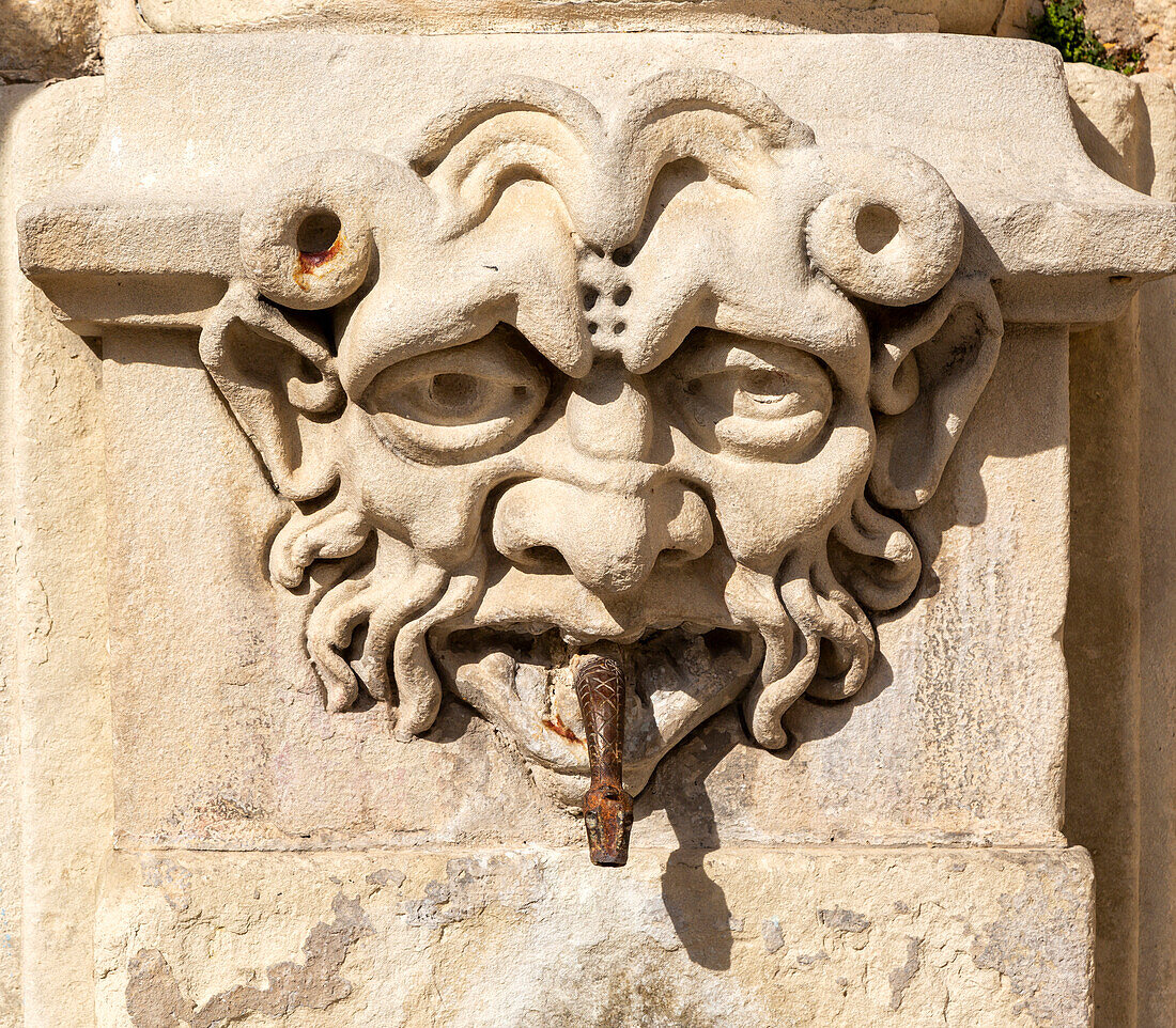 Geschnitztes Steingesicht auf altem Brunnen in Cuenca, Kastilien-La Mancha, Spanien, aus dessen Mund eine Schlange auftaucht