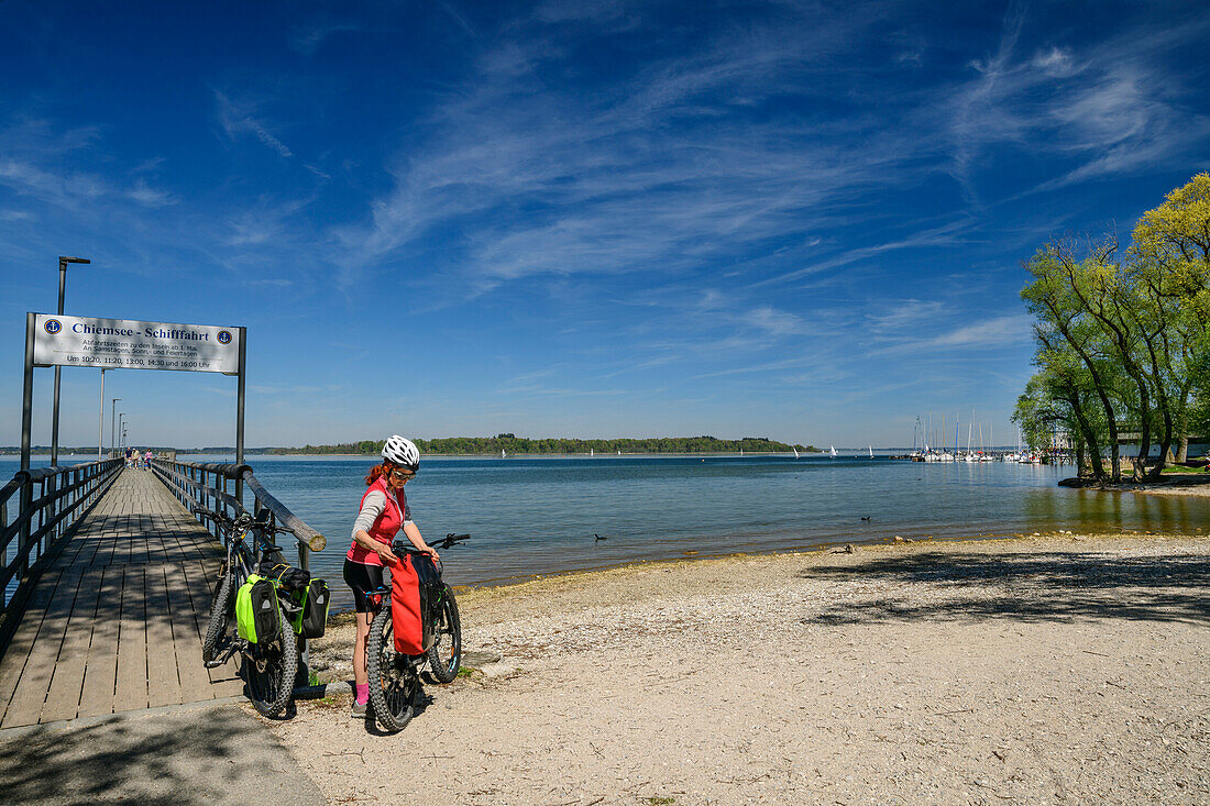  Woman cycling standing at jetty on Lake Chiemsee, Felden, Lake Constance-Königssee cycle path, Upper Bavaria, Bavaria, Germany 