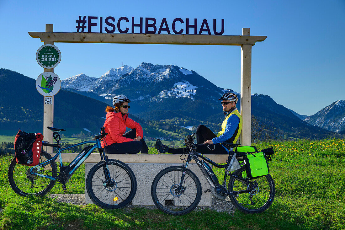  Man and woman cycling sitting at picture frame with Mangfall Mountains in the background, Lake Constance-Königssee cycle path, Fischbachau, Leitzachtal, Upper Bavaria, Bavaria, Germany 