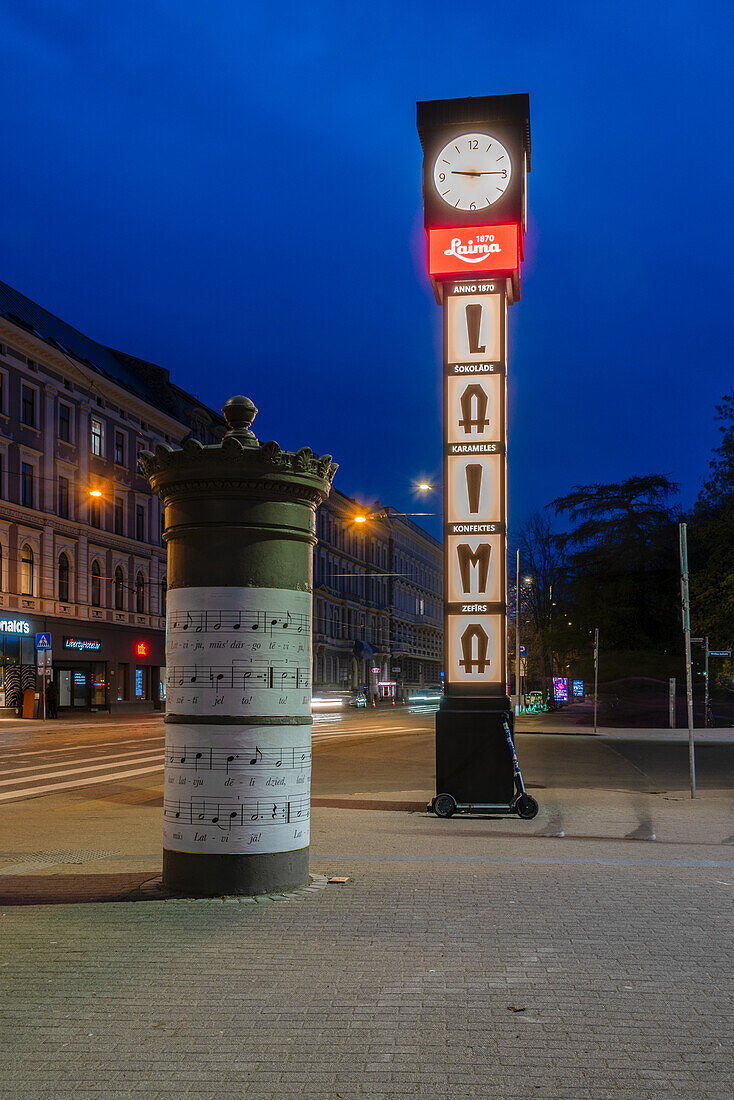 Laima-Uhr, Uhr der traditionellen lettischen Schokoladenfabrik Laima, davor Litfaßsäule mit Noten, Riga, Lettland