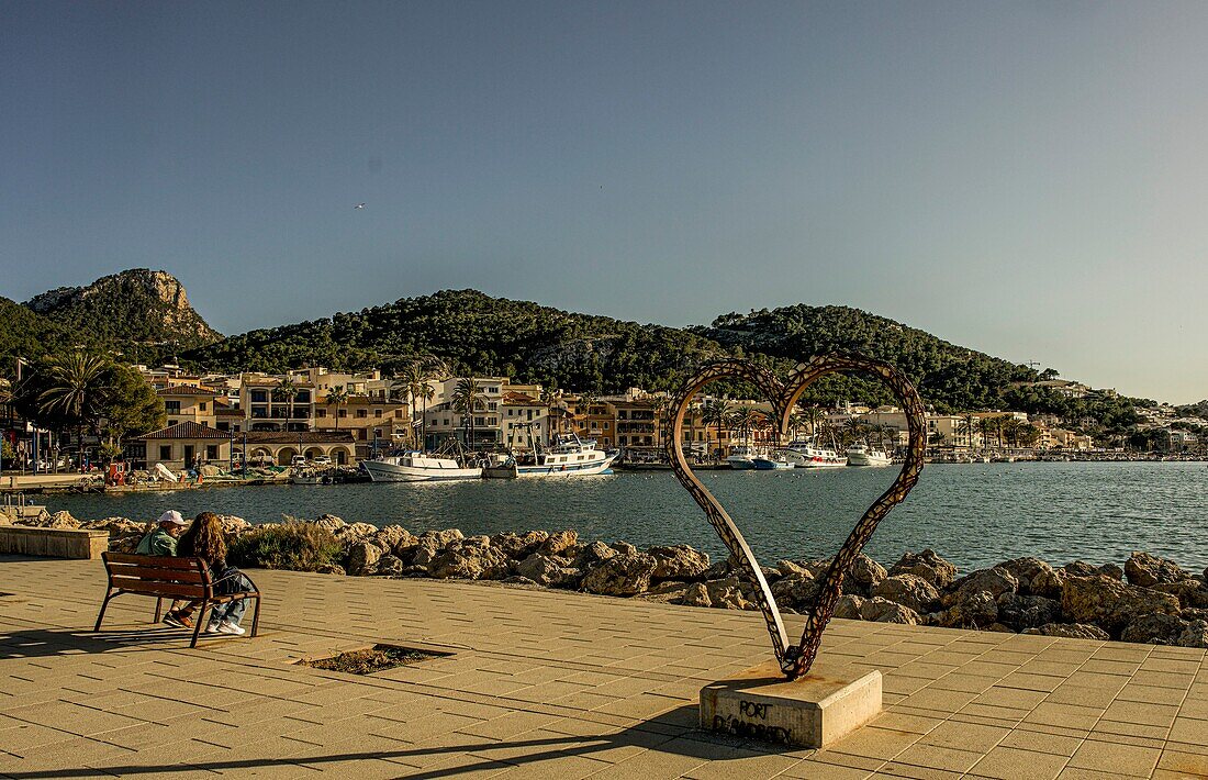  Sea promenade of Port d´Andratx, couple on bench, sculpture by Carlos Terroba, view of the harbor and the Tramuntana mountains, Mallorca, Spain 