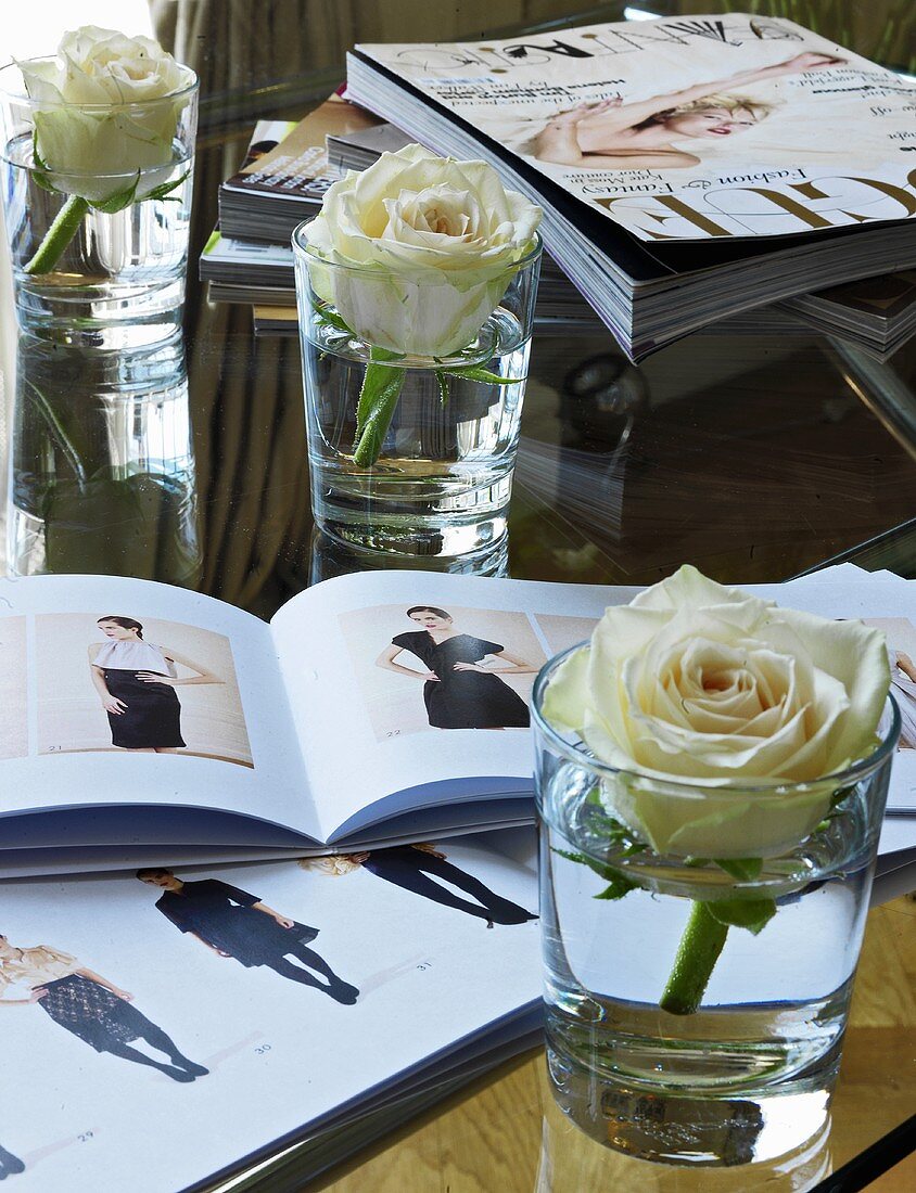 A rose in a glass of water next to a fashion magazine