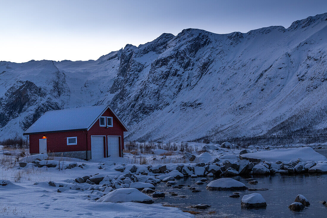 Winter in der Region Trömso, Tromvik, typisches traditionelles Haus mit Bergen im Dämmerungslicht