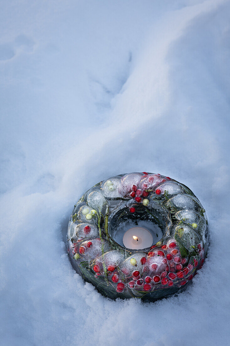 Weihnachtsdekoration mit Eisring in Kuchenform, gefüllt mit Stechpalme, Mistel, Zapfen und Nadeln im Schnee