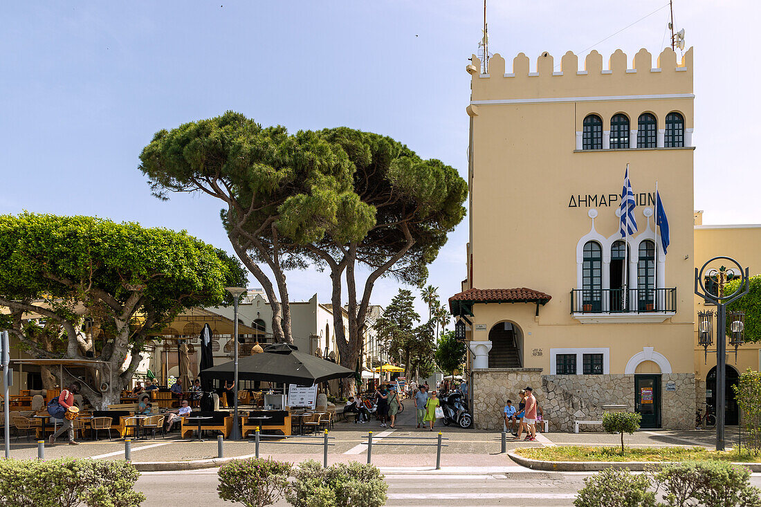 Rathaus, Restaurants und Altstadtgasse mit Fußgängern an der Hafenpromenade von Kos-Stadt auf der Insel Kos in Griechenland