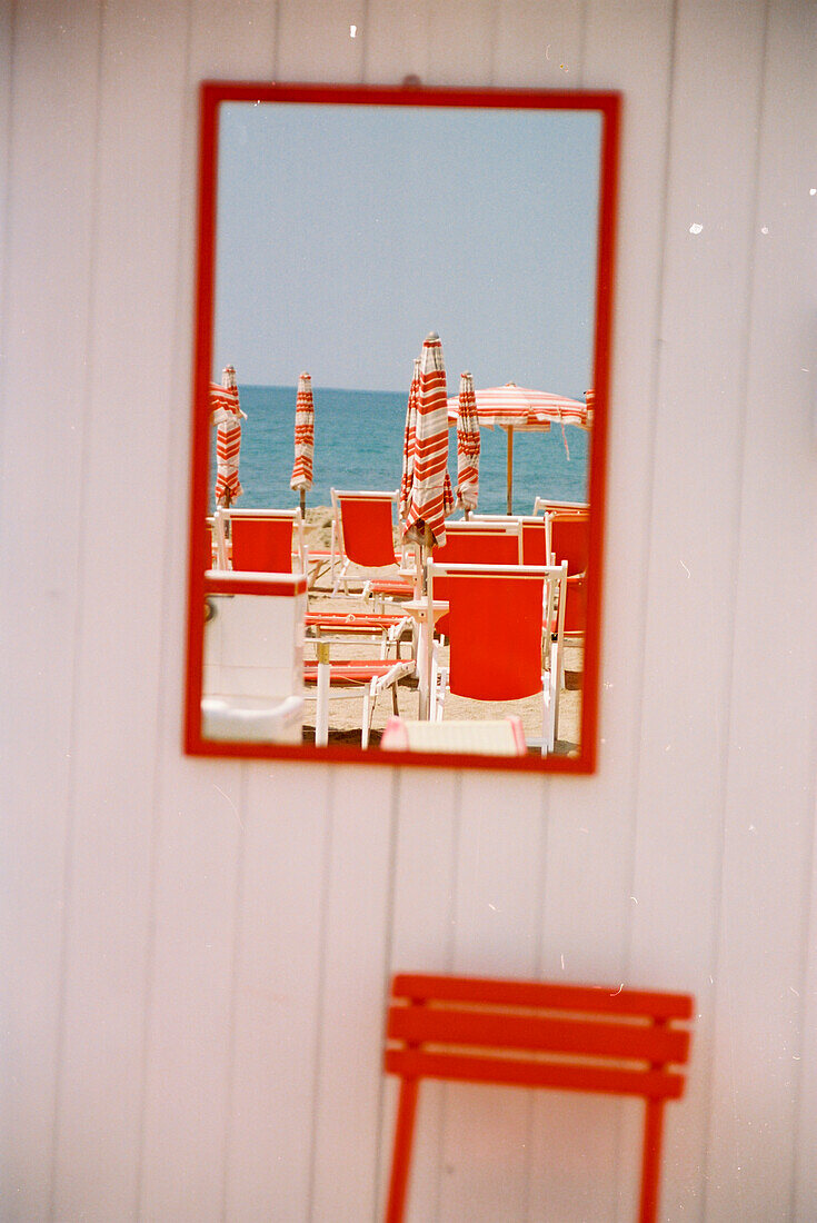 Rote Liegestühle spiegeln sich in Wandspiegel an Strandhütte, Ligurien, Italien