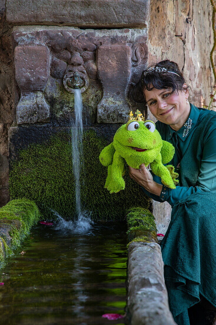 Frau im Kostüm der Figur „Prinzessin“ aus dem Märchen „Der Froschkönig“ der Brüder Grimm posiert am Brunnen, Steinau an der Straße, Spessart-Mainland, Hessen, Deutschland