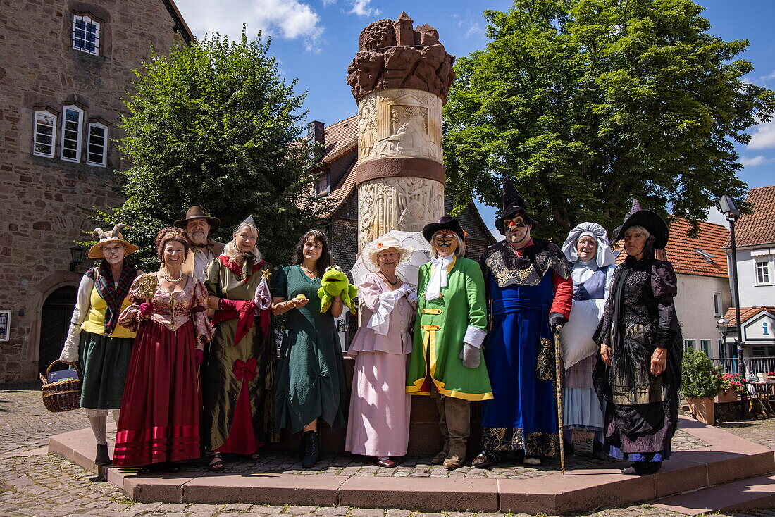  Locals in costumes of fairy tale characters from the Brothers Grimm pose in front of the fairy tale fountain in the old town, Steinau an der Straße, Spessart-Mainland, Hesse, Germany 