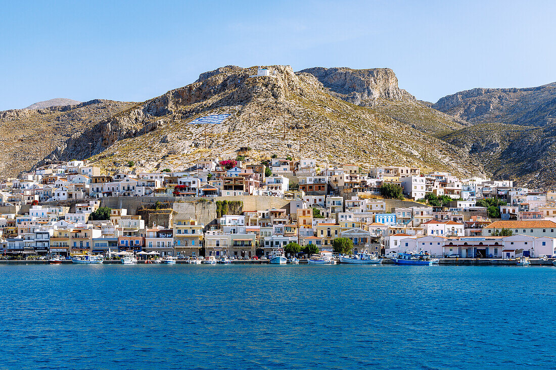 Inselhauptstadt Póthia, weiße Kapelle und gemalte griechische Flagge auf dem Hügel über Pothia mit Jachthafen auf der Insel Kalymnos (Kalimnos) in Griechenland