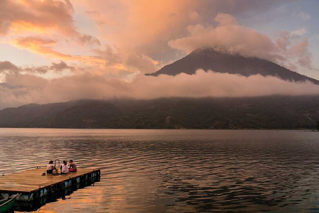  Touristen an einem Liegeplatz genießen den Sonnenuntergang, den Atitlan-See und den Vulkan San Pedro, Santiago Atitlan, Departement Sololá, Guatemala 