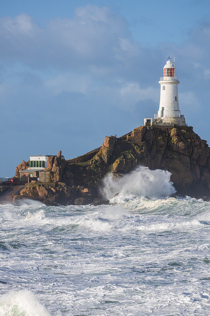  La Corbiere lighthouse on a rocky island during a storm, high tide. High waves crash against rocks. 