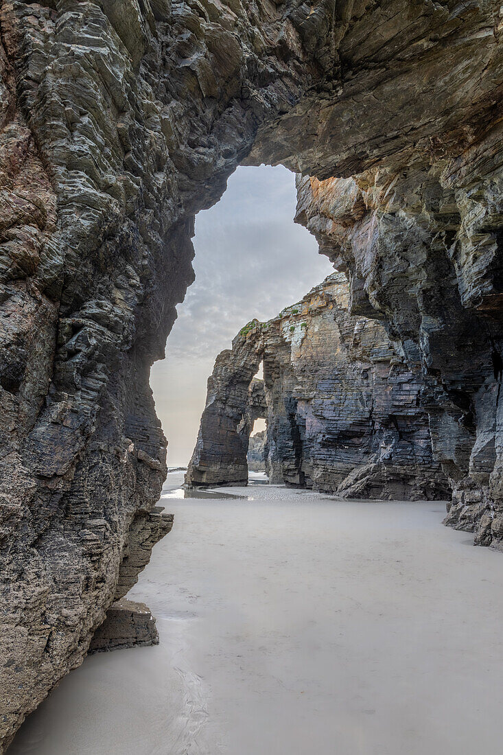  View through a rock arch on the sandy beach of Playa de las Catedralas. Deserted 