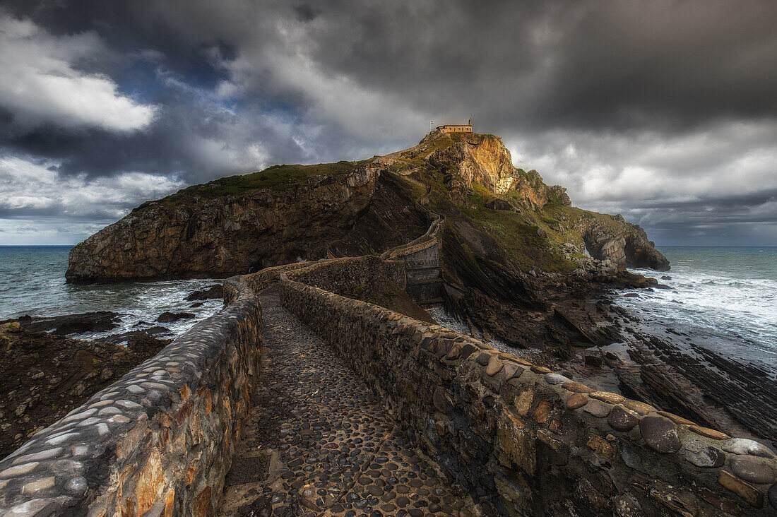  View of the path and the rocky island of San Juan de Gaztelugatxe under dark clouds. 