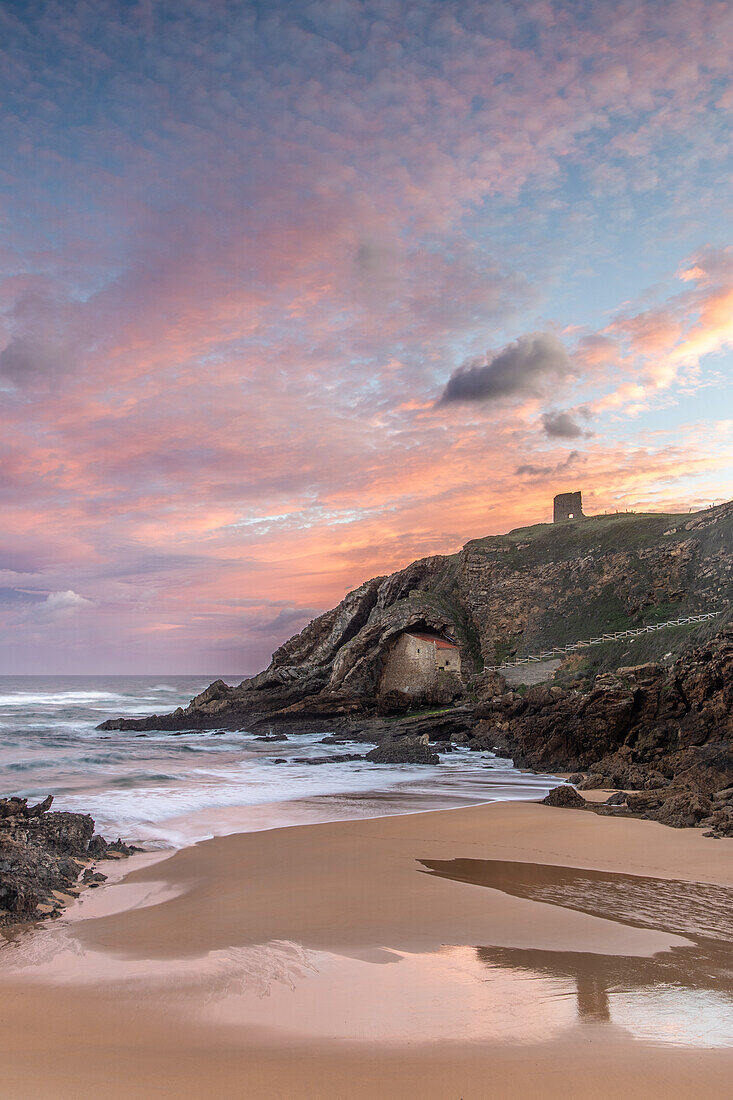  View over the beach to the rock chapel Ermita de Santa Justa. Blue and pink sky. 