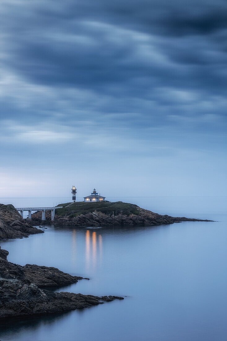  Blue hour. Calm sea. Rocky coast with a view of the Fara de Ribado lighthouse. 