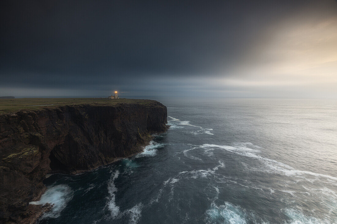  High cliffs by the sea with Stennes lighthouse at dusk. 