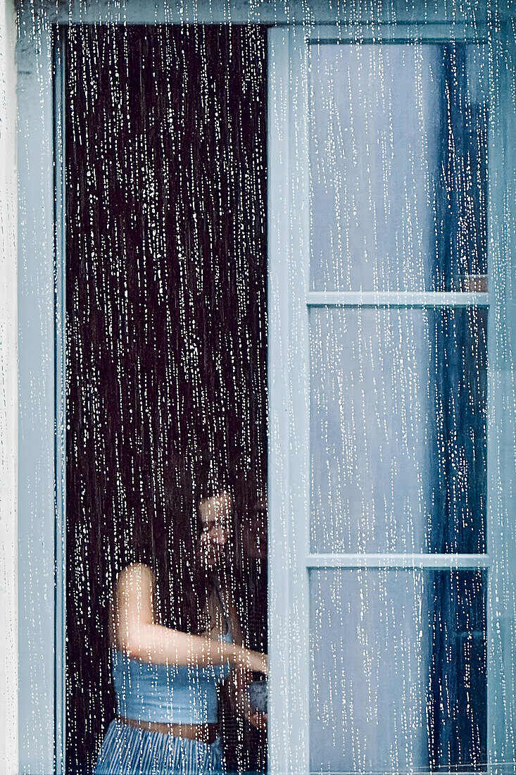 Mädchen am offenen Fenster hinter strömenden Regen in München, Bayern, Deutschland