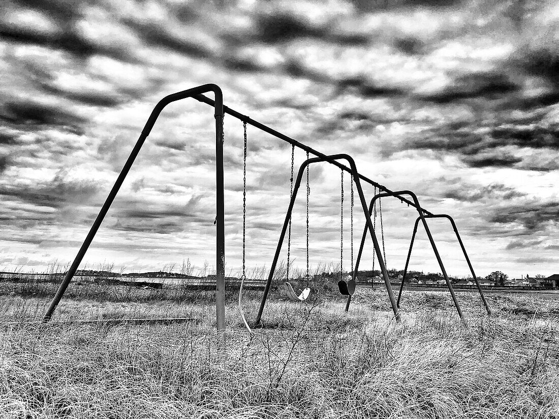 Swing set in field with long grass and dramatic sky