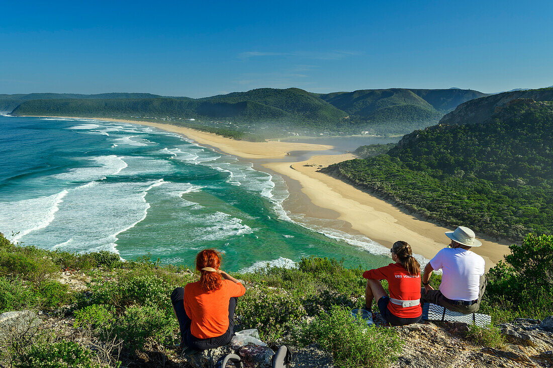  Three people sitting on a hill overlooking the sandy beach of Nature&#39;s Valley, Otter Trail, Tsitsikamma Section, Garden Route National Park, Eastern Cape, South Africa 