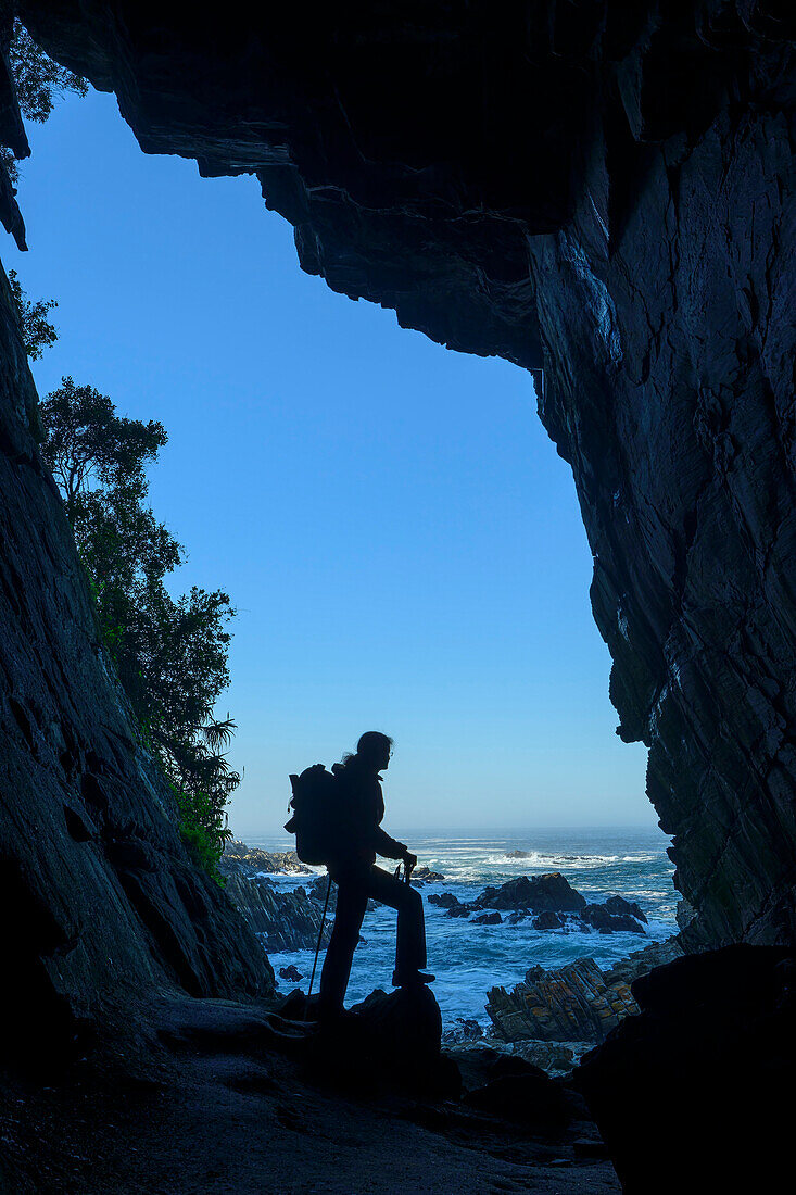  Woman hiking standing in Guano Cave and looking out to sea, Otter Trail, Tsitsikamma Section, Garden Route National Park, Eastern Cape, South Africa 