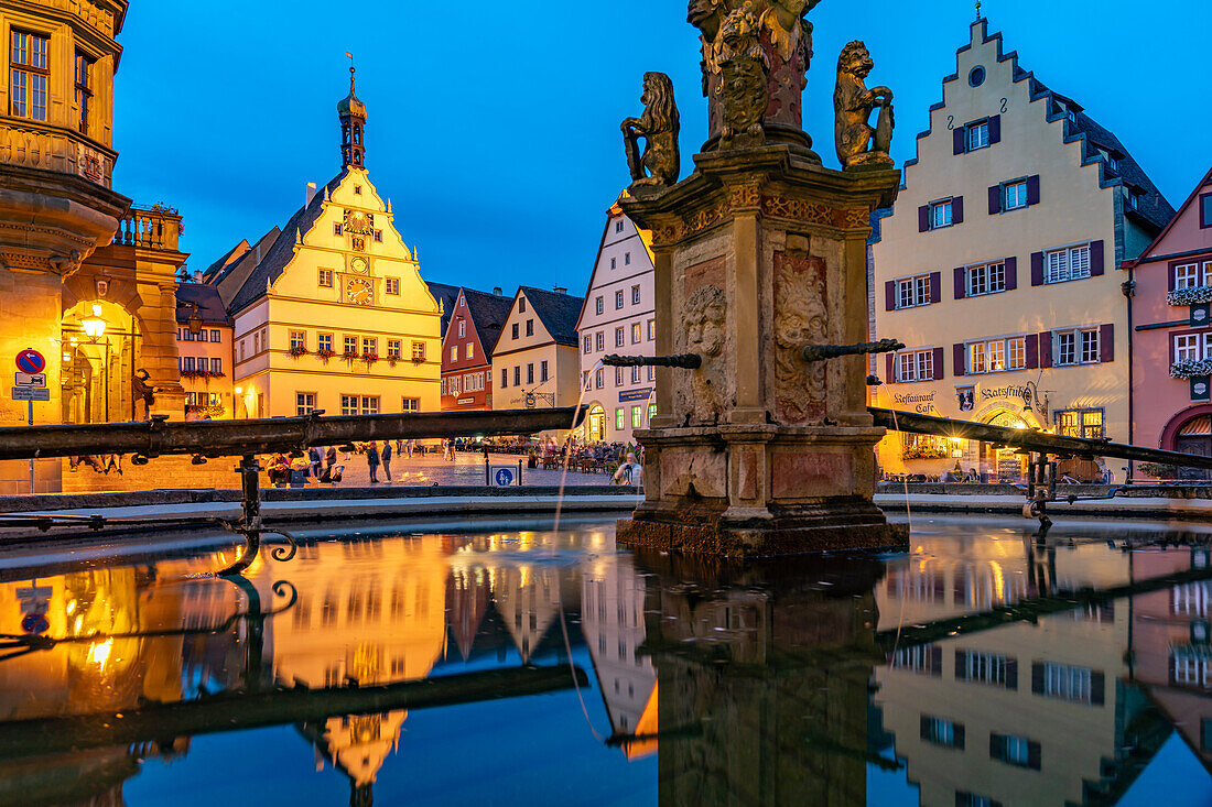 Der Marktplatz mit Ratstrinkstube spiegelt sich im Georgsbrunnen in der Abenddämmerung, Rothenburg ob der Tauber, Bayern, Deutschland 