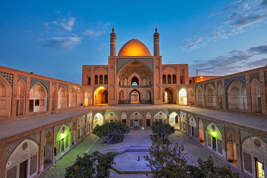 Blick auf die Agha-Bozorg-Moschee aus dem 18. Jahrhundert und ihren Innenhof, beleuchtet in der Abenddämmerung. Kashan, Iran.