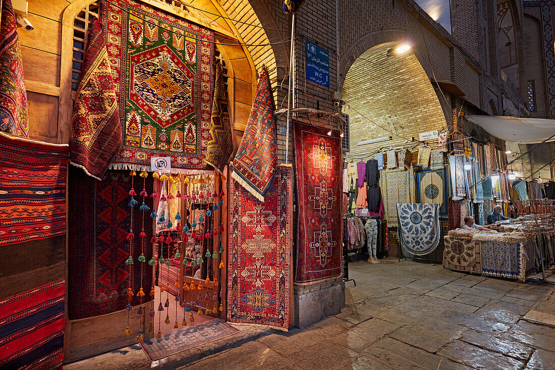 A selection of handmade Persian carpets displayed at the entrance of a handicraft shop in Naqsh-e Jahan Square illuminated at night. Isfahan, Iran.