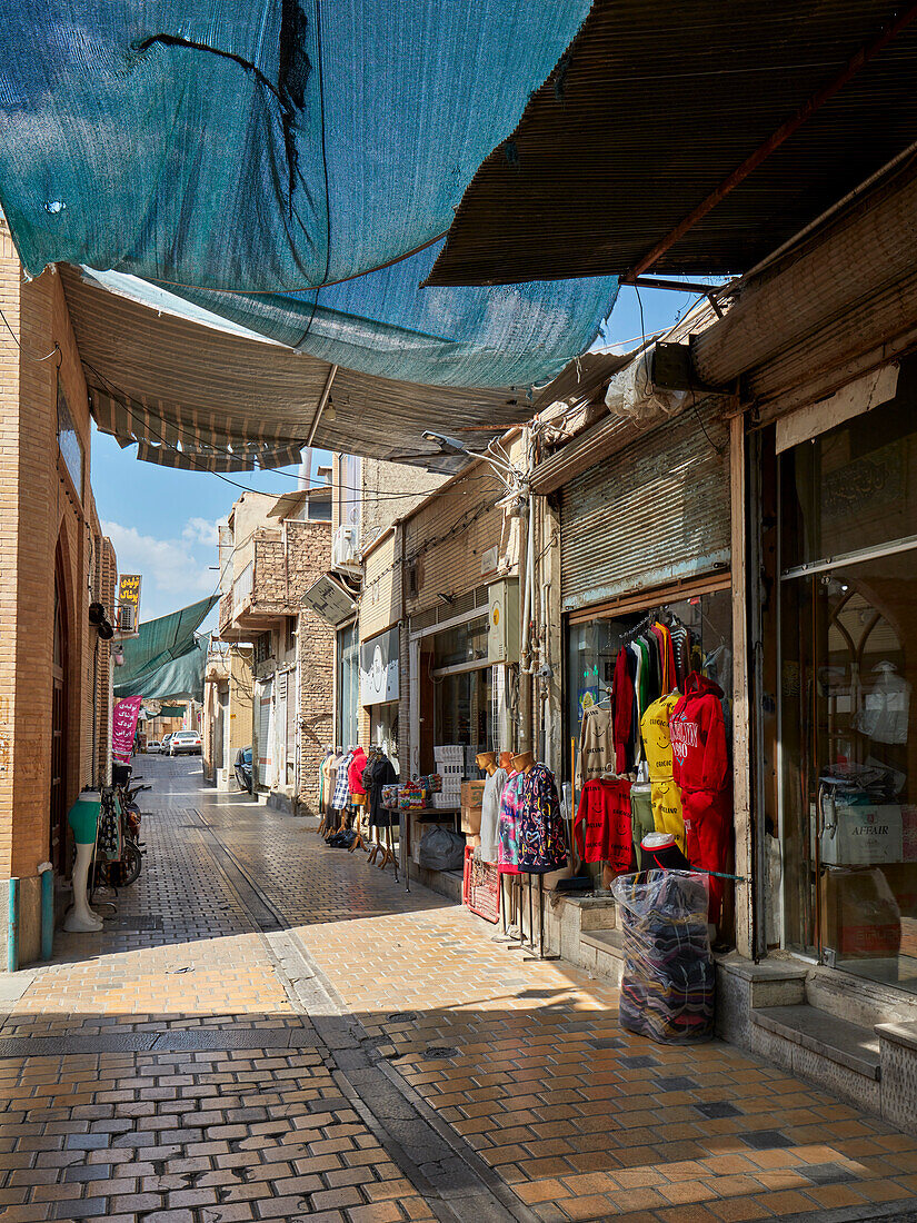 A narrow cobbled street with sun shade canopy lined with small shops in the historic center of Isfahan, Iran.