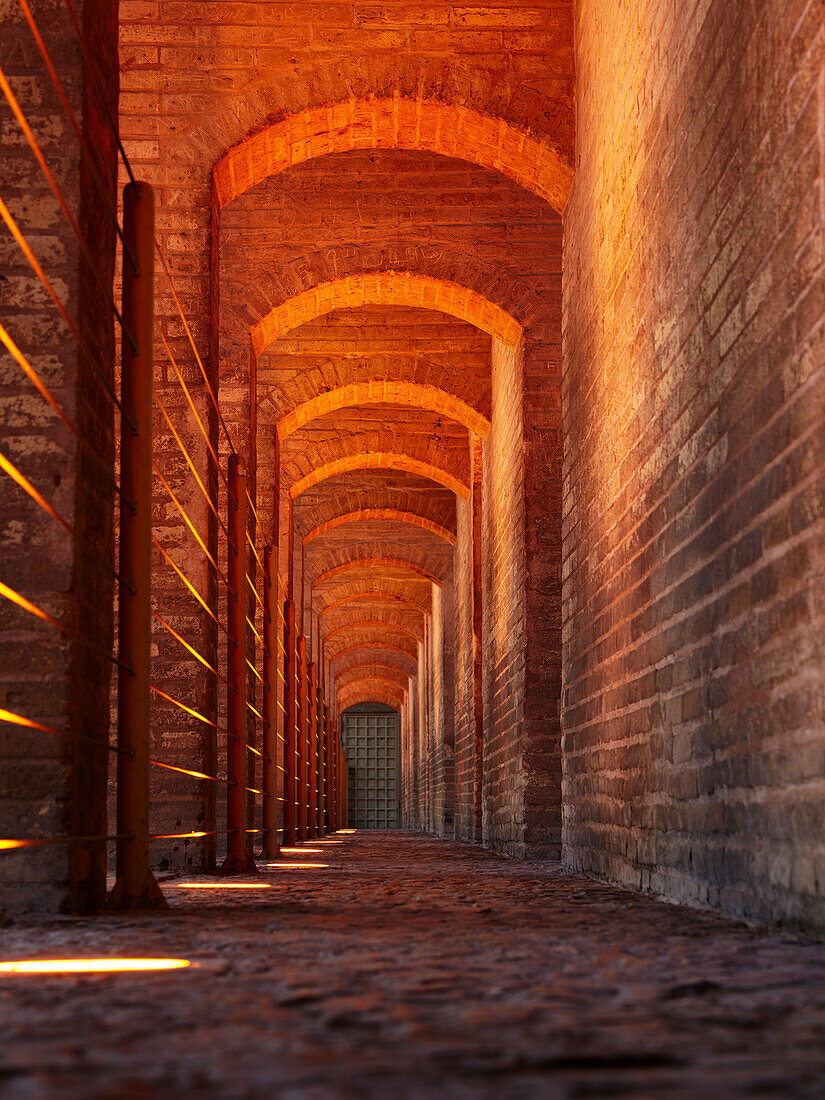 A low angle view through illuminated vaulted arches of the 17th century Khaju Bridge on Zayanderud river in Isfahan, Iran.