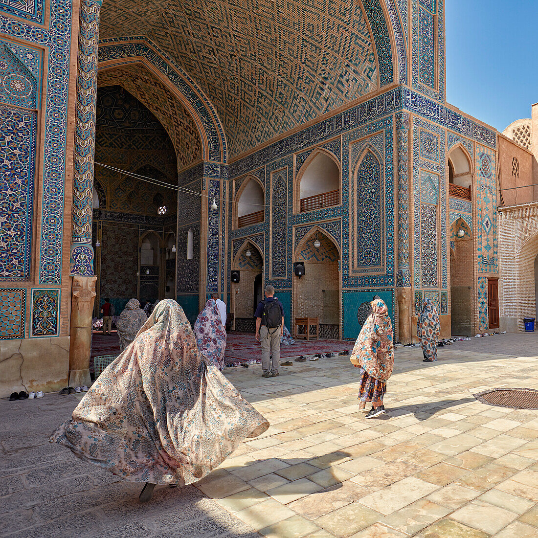  Eine Frau mit ihrem im Wind wehenden Tschador geht zum Eingang der Jameh-Moschee von Yazd, einer schiitischen Moschee aus dem 14. Jahrhundert in der Altstadt von Yazd, Iran. 