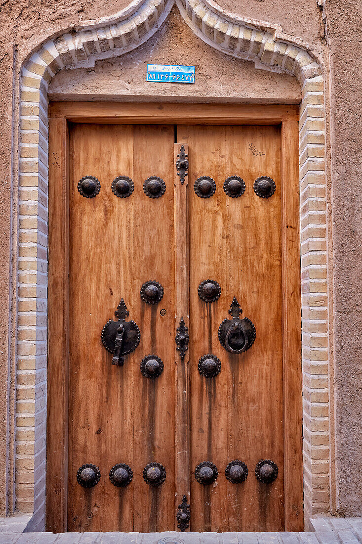 Traditional wooden front door with two separate knockers - metal bar for men and metal ring for women. Yazd, Iran.