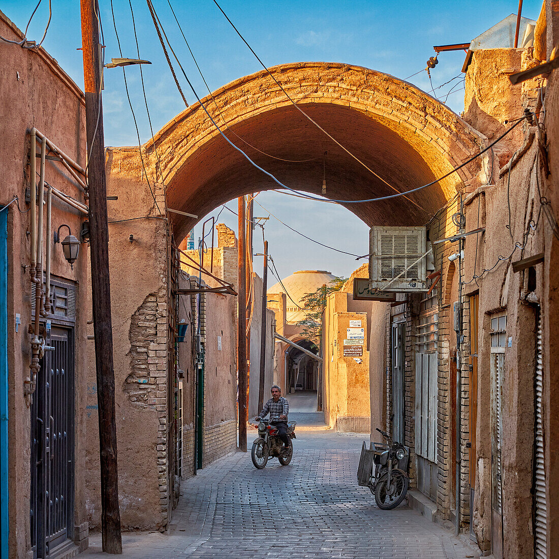 A man on motorbike rides in a narrow street through an archway in the historical Fahadan Neighborhood of Yazd, Iran.